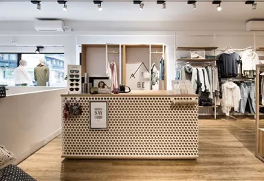 Ein moderner Bekleidungsladen mit einem hellen Empfangstresen. Die Wände sind mit diverse Kleidung und Accessoires dekoriert.