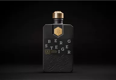 Eine stilvolle Flasche mit schwarz-goldenem Design. Auf der Flasche sind die Buchstaben "Bergsteiger" in moderner Schrift angeordnet.