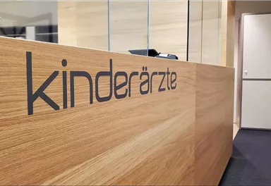 A reception desk in a pediatric practice. The decorative wood surface and the clearly readable inscription "pediatricians" create an inviting atmosphere.