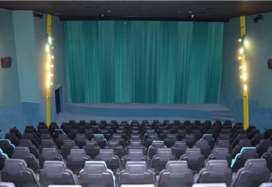 An empty cinema hall with black seats and a blue curtain. The lighting creates a cozy atmosphere.