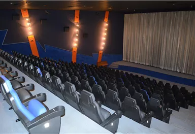 An empty cinema hall with comfortable seats and a stage in the background. The walls are decorated in blue with lights.