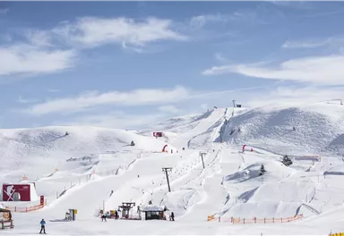 Eine verschneite Landschaft mit Skiliften und Pisten. Der Himmel ist klar und blau, ideal für einen Skitag.