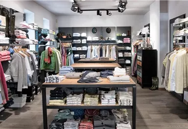 Ein gut sortierter Bekleidungsladen mit Regalen voller Kleidung. Es gibt mehrere Tische mit sorgfältig gefalteten Kleidungsstücken.