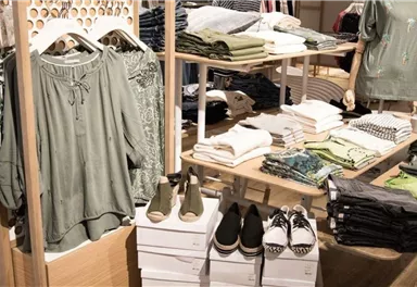 Ein stilvolles Warensortiment mit Kleidung in verschiedenen Grüntönen und Schuhen. Die Produkte sind neatly auf Regalflächen angeordnet.