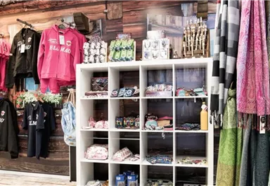 Ein Verkaufsregal mit verschiedenen Textilien wie Sweatshirts, T-Shirts und Schals in einem Geschäft. Im Hintergrund sind weitere Kleidungsstücke und Accessoires zu sehen.