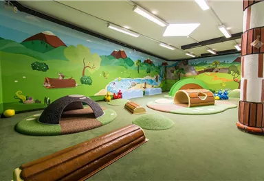 A large play area with colorful mats and play structures. On the wall, there are cheerful, child-friendly landscape pictures.
