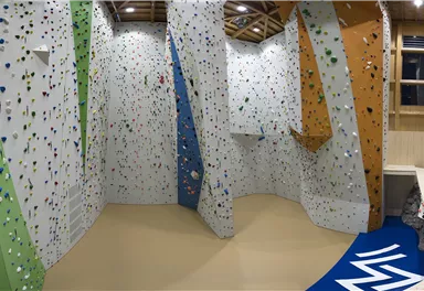 Eine moderne Kletterwand mit bunten Griffen und verschiedenen Schwierigkeitsgraden. Der Raum ist gut beleuchtet und bietet Platz für Kletterer.