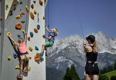 A climbing tower in the mountains, where children climb. Impressive mountain landscapes can be seen in the background.