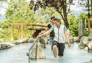 Two women are walking in the warm water of a natural pool. Surrounded by trees and rocks, they enjoy the relaxing atmosphere.