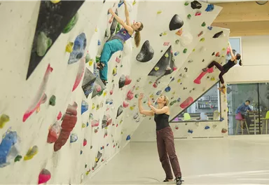A climbing gym with several people training on a climbing wall. The atmosphere is active and sporty.