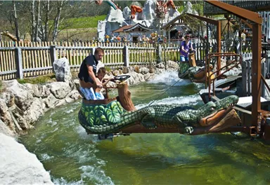 A family activity in a water park with a frog ride. Children and adults enjoy the ride in a green, reptile-like attraction.