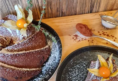 A delicious chocolate cake on a plate, decorated with fruit and powdered sugar. Next to the cake is a piece of cake on another plate, ready to be enjoyed.