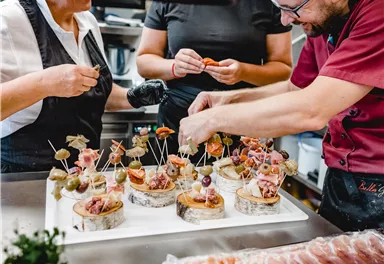 Eine Gruppe von Köchen bereitet kreative Snacks auf Holzplatten vor. Die farbenfrohen Häppchen sind mit Holzspießen dekoriert.