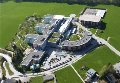 A modern building complex in a green landscape. The structure includes several separate buildings and is surrounded by lawns.