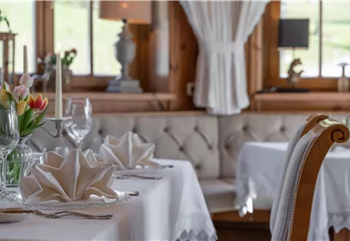 An elegant restaurant with beautifully set tables and fresh flowers. The bright windows let in plenty of light and create an inviting atmosphere.