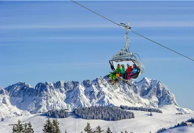 A group of skiers is riding in a gondola over snow-covered mountains. The clear sky and the stunning landscape create a winter atmosphere.