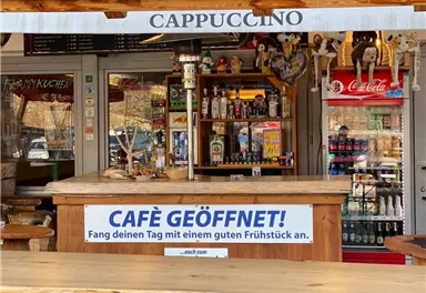 A café with a wooden bar and drinks. A sign states that the café is open and offers breakfast.