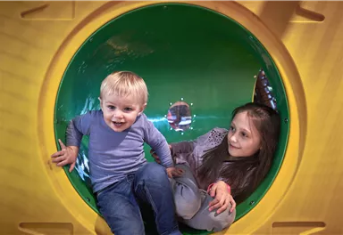 A little boy and a girl are playing together in a colorful tunnel. Both are joyful and laughing.