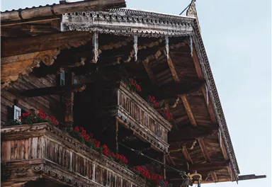 Ein traditionelles Holzhäuser mit geschmückten Balkonen und bunten Blumen. Der Himmel ist klar und die Architektur zeigt einen typischen regionalen Stil.