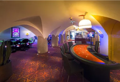 An elegant casino with a stylish gaming table and dimmable lighting. In the background, gaming tables and machines are visible.