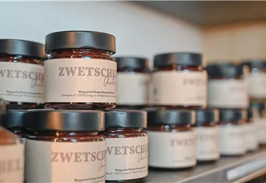 Ein Regal mit mehreren Glasbehältern, die Zwetschgenmarmelade enthalten. Die Etiketten sind schlicht und beschreiben den Inhalt.