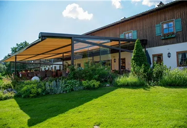 A cozy house with a large terrace and a bright sunshade. The garden is green and lush, with many plants and seating areas.