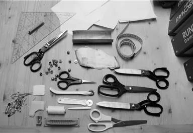 A collection of cutting and sewing tools on a table. Among them are scissors, sewing thread, a template, and numerous small objects.