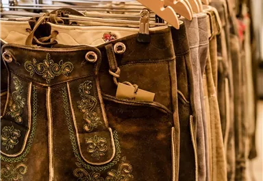 Eine Auswahl an traditionellen Lederhosen hängt an Holzkleiderbügeln. Die Hosen sind kunstvoll verziert und aus hochwertigem Material gefertigt.