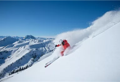 A skier is skiing through fresh snow in the mountains. The sky is clear and blue, and the landscape is impressive.