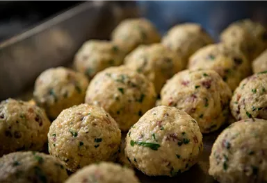 A collection of small, round dumplings, prepared with herbs and other ingredients. They rest on a metal plate and seem ready to be served.