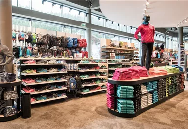 Ein modernes Sportgeschäft mit Kleidung und Ausrüstung. An Regalen sind bunte Waren ordentlich präsentiert.