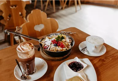 A delicious breakfast with a colorful bowl of granola, fresh fruits, and yogurt. Accompanied by a cappuccino and a cup of coffee with whipped cream.