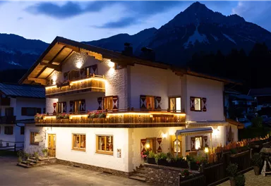 Ein gemütliches Chalet mit warmem Licht, umgeben von majestätischen Bergen. Die Dunkelheit hebt die Schönheit des Hauses hervor.