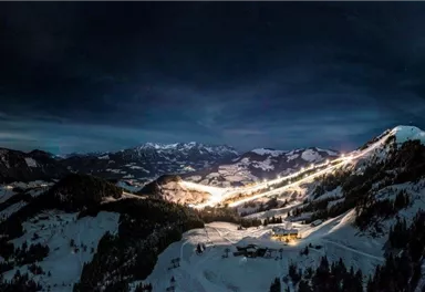 An impressive nighttime Alpine landscape with snow-covered mountains. Lights from ski resorts create a moody atmosphere.