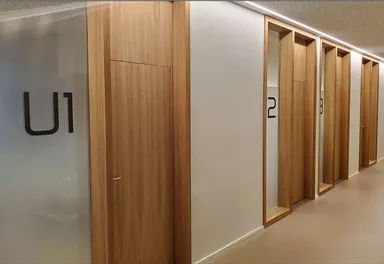 A modern hallway with wooden paneling and clear glass doors. Visible numbering on the doors indicates different rooms.