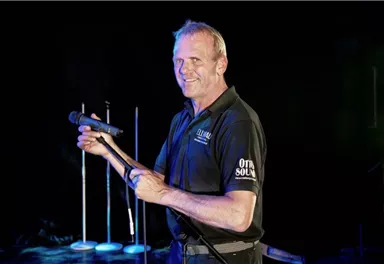 A man stands on a stage holding a microphone in his hand. He is smiling and seems ready for a performance.