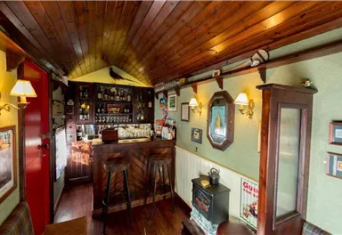 A cozy pub with wooden paneling and a small bar counter. The walls are adorned with artworks and decorative elements.