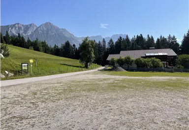 An idyllic landscape with gentle hills and high mountains in the background. In the foreground stands a typical alpine building.