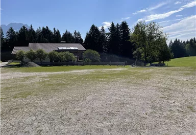 A spacious property with a meadow and scattered trees. In the background, a house can be seen, surrounded by a tranquil natural landscape.