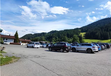 A parking lot with several cars and a beautiful mountain landscape in the background. The sky is clear with some clouds.