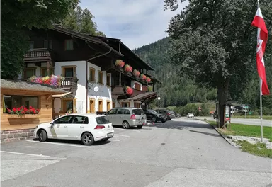 An idyllic village with traditional wooden houses and blooming balconies. In the background, green mountains and a clear sky can be seen.