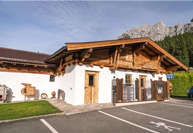 A traditional chalet with wooden cladding in a picturesque setting. In the background, you can see impressive mountains and a green meadow.