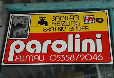 A sign for a plumbing and heating company. It displays the company name "parolini" and contact information.