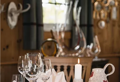 A stylishly set table with glasses, napkins, and a candle. In the background, wooden paneling and decorative elements are visible.
