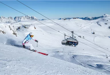 A skier glides through the fresh snow in the mountains. In the background, a ski lift is visible.
