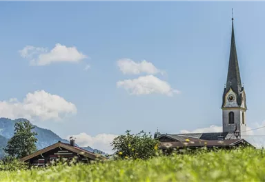 A picturesque landscape with a church and a typical chalet. The sky is blue and interspersed with some clouds.