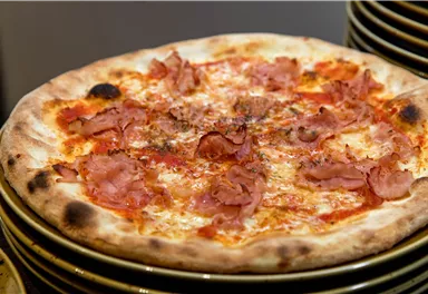 Eine köstliche Pizza mit Schinken und geschmolzenem Käse. Sie liegt auf einem Stapel von Tellern.