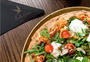 Eine frisch gebackene Pizza mit Rucola, Kirschtomaten und Mozzarella. Daneben liegt eine Serviette auf einem Holztisch.