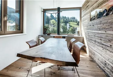 Ein modern gestalteter Essbereich mit einem Holztisch und braunen Stühlen. Große Fenster bieten einen Blick auf die umliegenden Berge und die Natur.