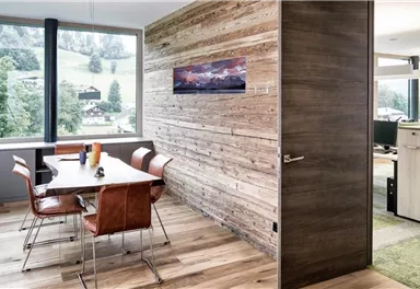 Ein moderner Büroraum mit einem großen Fenster und Blick auf die Natur. Der Tisch ist mit eleganten Stühlen ausgestattet und die Wände sind aus Holz gefertigt.